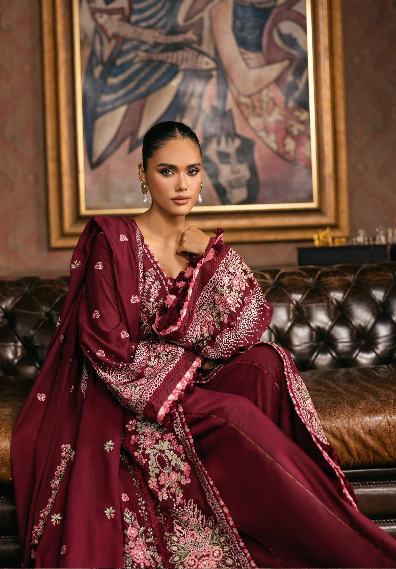 Woman in a burgundy embroidered traditional outfit sitting on a leather couch.