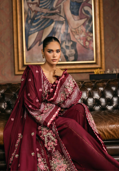 Woman in a burgundy embroidered traditional outfit sitting on a leather couch.
