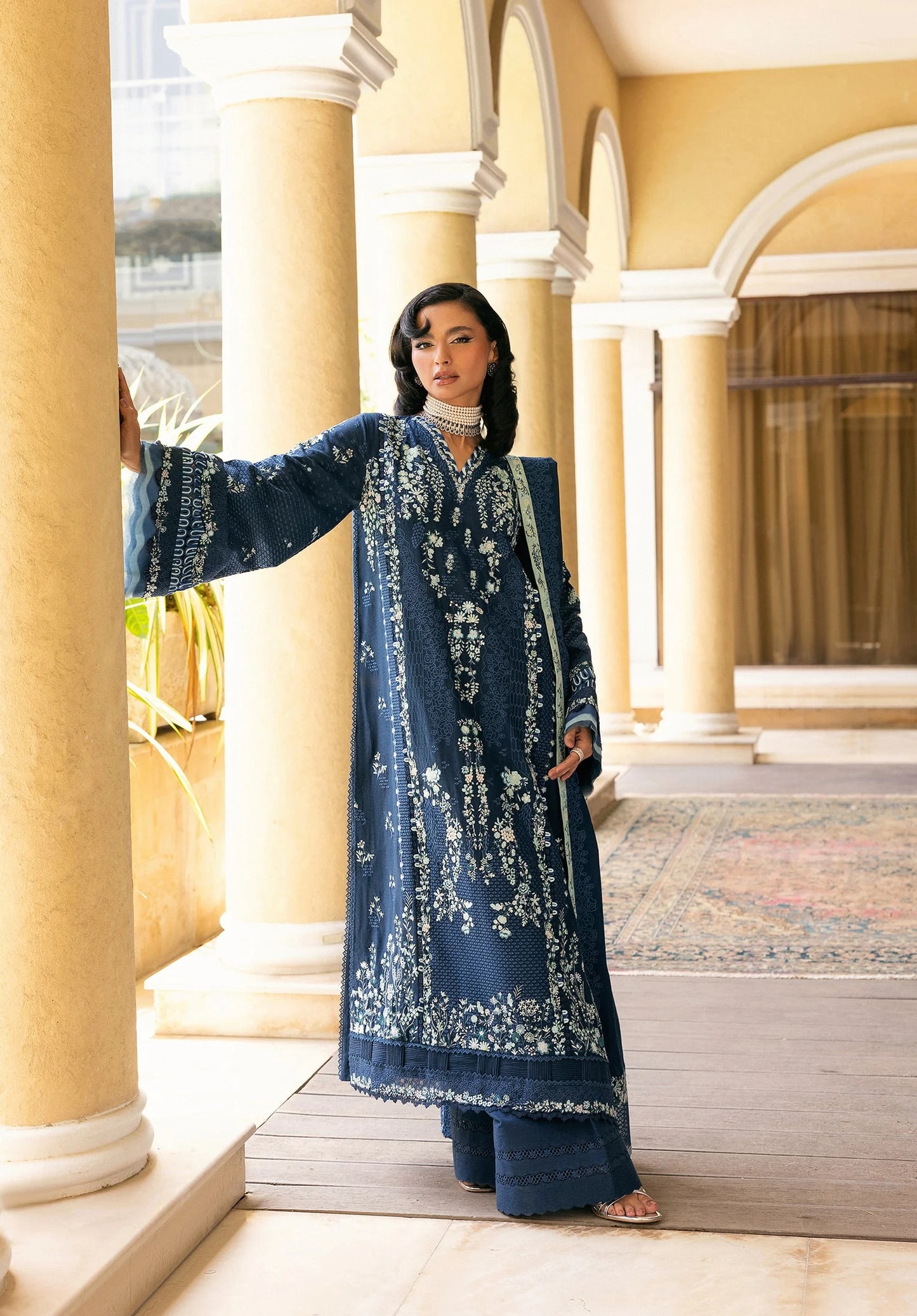 Woman in a blue embroidered traditional outfit standing in an architectural setting with ELAF LUXURY WINTER