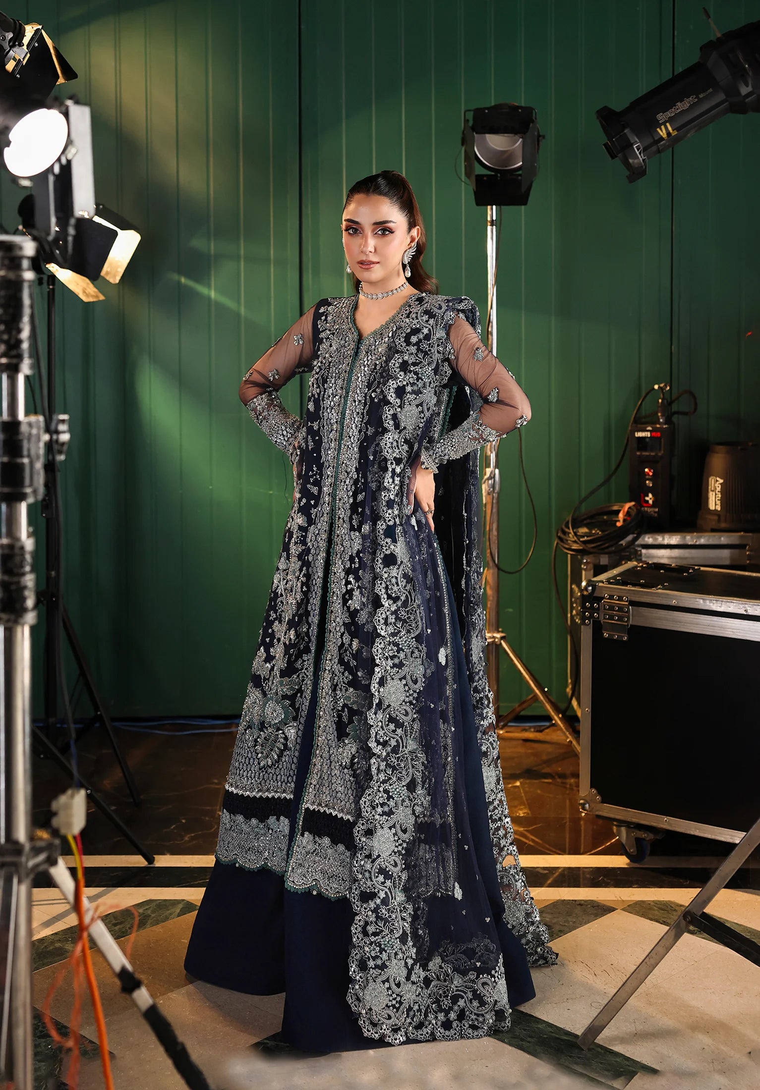 Woman in a dark blue and white floral traditional outfit standing in a photo studio with green screen background with Elaf Stardom Handwork.