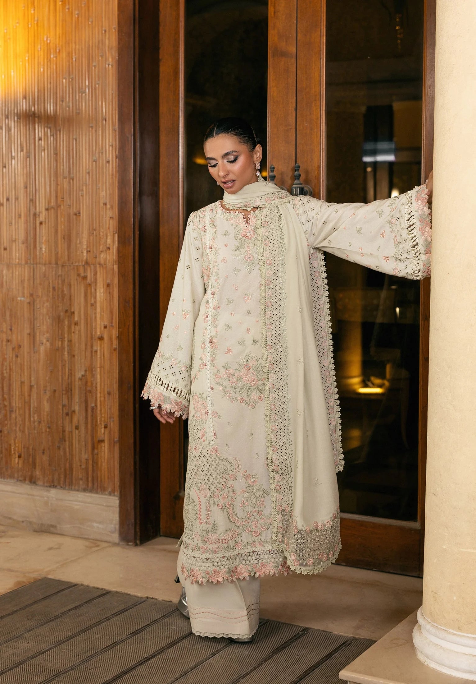 Woman in a cream embroidered traditional outfit standing indoors.